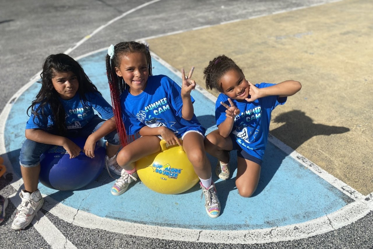 three students at PBMA charter school smiling together on the outdoor playground